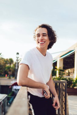 Barcelona 'da deniz kenarındaki ahşap çitlere yaslanırken ışıl ışıl gülümseyen gündelik giysiler içinde mutlu bir adamın yan görüntüsü.