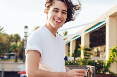 Neşeli Milenyum turisti, akıllı telefon cihazıyla seyahat sitesinde blog yazarken eğleniyor. Cep telefonunda 4G kullanan zengin bir hipsterin yarım boy portresi.