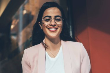 Eğitim kitabı ve kahvesi olan zeki bir bayan öğrenci kameraya gülümseyecek. Optik gözlüklü neşeli İspanyol kadının yarım boy portresi kaldırımda bilgi öğreniyor.