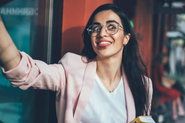 Ders kitabı yazan komik kadın şair molada cep telefonu ön kamerasını kullanarak selfie çekerek fotoğraf çekiyor. Gözlüklü neşeli Gürcü kadın kaldırımda pozitif video çekiyor.