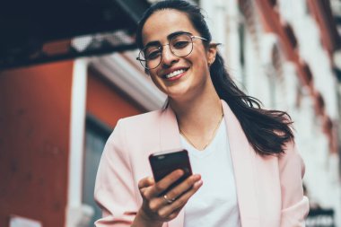 İspanyol gezginlerin yarım boy portresi elinde kafein içeceği ve mobil teknolojisiyle şehri ziyaret ederken kameraya gülümsüyor, gözlüklü mutlu hippi kız yemek kupası ve cep telefonu ile poz veriyor.