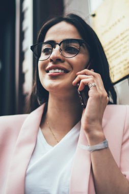 Görme düzeltmesi için optik gözlüklü güzel İspanyol kullanıcı boş zamanlarında uluslararası telefon konuşmalarından keyif alıyor, pozitif iletişim kurmak için aylak aylak dolaşan gözlüklü çekici kadın.