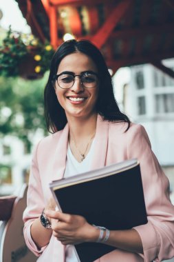 Şehir merkezinde poz veren neşeli kadın gazetecinin yarım boy portresi, klasik gözlüklü başarılı Gürcü kadın şehirde boş zamanlarında kameraya gülümsüyor.