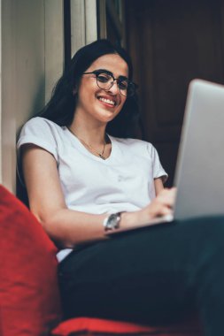 Klasik gözlüklü yetenekli bir işçinin portresi modern dizüstü bilgisayarla koltukta oturuyor ve kameraya gülümsüyor, bilgisayarlı neşeli İspanyol metin yazarı serbest yaşam tarzından keyif alıyor.