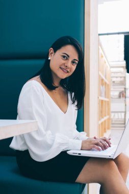 Barcelona Kafe 'de dizüstü bilgisayarla çalışırken şık giyinen, gülümseyen ve kameraya bakan çağdaş esmerin yan görüntüsü