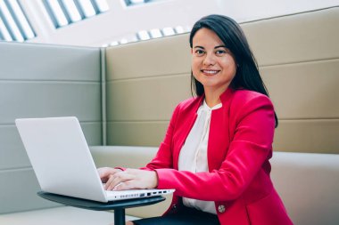 Beyaz bluzlu ve siyah etekli etnik kadın koltukta oturuyor cep telefonu rehberi ile ve parlak ofiste çalışmanın tadını çıkarıyor.