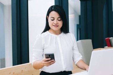 Resmi giysiler içinde genç bir bayan girişimci kütüphanede bilgisayarla çalışırken masada oturup akıllı telefonlara göz attığı için memnunum.