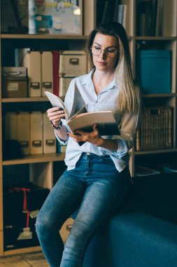 Genç çekici yetenekli kız öğrenci zamanı kitaplığı harcama yaklaşan sınavlar için hazırlanıyor modaya uygun kıyafet giymiş. Şirin hippi kız rahat koltukta otururken bilgilerini gözden