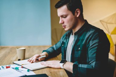 Genç adam akıllı erkek öğrenci ile kağıt ve Kırtasiye kafede oturan üniversite sınavları için hazırlık kurs projesinin planlama iç yapım coworking uzayda öğrenme konsantre