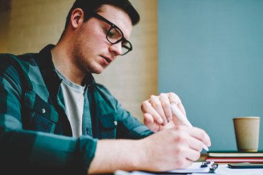 Dalgın zeki erkek öğrenci üniversitede, konsantre hipster adam kontrol zaman organizasyon öğrenme sürecinde üniversite sınavına hazırlık testi test yazma sırasında kol saati seyir