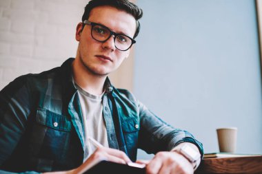 Gözlük vizyon düzeltme mesafe iş sürecinde, profesyonel erkek serbest kamera Cafe bakarak yayın makaleleri notlar yapmak için ciddi hipster adam portresi