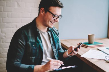 Komik video gülen neşeli genç adam Smartphone'da uzaktan kafede, çalışırken göz hipster adam üstünde email tebliğ üstünde telefon kontrol iyi haber alma ile memnun gülümsüyor