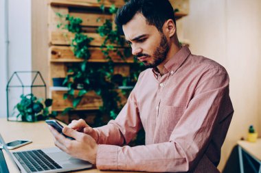 Ciddi genç erkek freelancer uzay coworking oturan smartphone posta denetlerken kötü haber ile hayal kırıklığına uğrattı, hipster adam bankacılık denge yolu ile cellphone üzerinde app okuma hakkında kızgın vurguladı