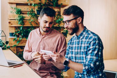Gülümseyen hippi çocuklar dijital tablet ve modern uygulamalar kullanarak boş zamanlarını geçiriyorlar, sakallı erkek dokunmatik dokunmatik oyunlar oynuyor ve arkadaşlarıyla kampüste boş zamanlarında konuşuyorlar.