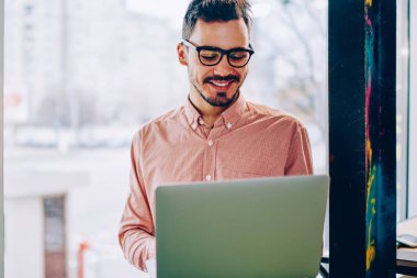 Genç hipster adam gözlük vizyon koruma dizüstü bilgisayar, netbook çalışma için iyi geri bildirimler hakkında mutlu neşeli erkek freelancer Gözat web sayfasında bilgi okumak için memnun
