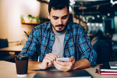 Bildirim gelir çıkıyor öğrenme için üniversite kafeteryada otururken hücresel, genç erkek yükleme uygulaması üzerinde cep telefonu sosyal ağlardan kontrol dalgın hipster adam