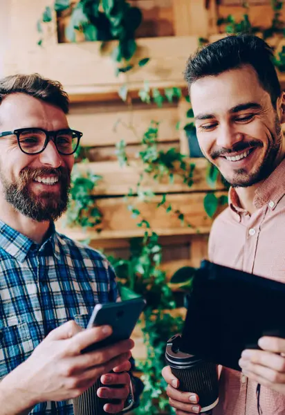 Neşeli hipster çocuklar birlikte gülüyor pay yolu ile bluetooth bağlantı, komik ortak fotoğraf kaygısız erkek öğrencilerin sosyal ağlar güncelleştirmelerini denetlemek için dijital cihazlar kullanarak birbirleri ile şaka