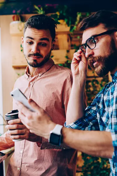 Duygusal hipster adam akıllı telefon bildirim seyir ve şok alış irsaliyesi bill, alma ile genç adam kötü getting haber cep üzerinde hayal kırıklığına duygu onun arkadaşıyla haber okuma vurguladı