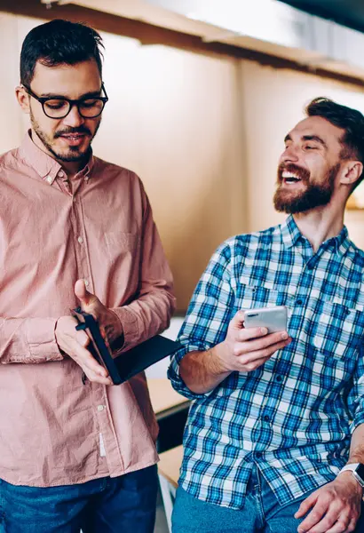 Genç gülümseyen hipster adam meslektaşım tarafından tatilinde ofiste, arkadaş onun komik resimler e-posta alma Smartphone'da ağ üzerinde şaka duygusal neşeli adam komik hikaye gülüyorsun