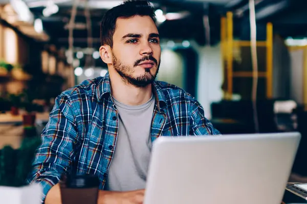 Düşünceli erkek freelancer uzay, netbook ve wifi öğrenme için üniversite kitaplığında kullanarak düşünceli genç öğrenci coworking içinde dizüstü bilgisayar ile oturup çalışma projesi için fikir üzerinde durulması