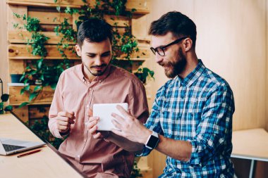 Genç hipsterlar yeni taşınabilir bilgisayarları ve ara verildiğinde ortak çalışma alanı içinde iletişim kuran uygulamaları kontrol ediyorlar, yetenekli geliştiriciler dijital tablet üzerindeki yazılımı güncellemekten memnun kalarak teknolojiyle ilgili fikirleri tartışıyorlar.