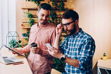Konsantre hipster adam telefonda gelir mesajı okurken arkadaşı ilginç, yetenekli iş arkadaşları modern teknolojiyi kullanarak iş birliği yapmayı planlıyorlar.