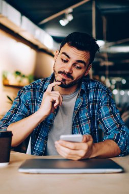 Düşünceli bir erkek, internet sitesinde yer ayırtma hakkında bilgi toplarken, kafası karışmış hipster adam, akıllı telefondan e-posta kontrol makbuzu almak için kafa yoruyor.