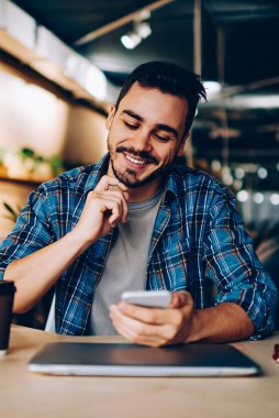 Sosyal ağlarda yeni mesajlar okuyan gülümseyen yenilikçi adam akıllı telefondan yeni bir arkadaşı doğruladı, cep telefonu bakiyesindeki bankacılık uygulamasından memnun olan genç adam öğrenirken cep telefonu bakiyesini kontrol ediyor.