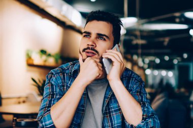 Düşünceli hippi adam telefonda konuşurken iş yerinde oturup düşünüyor. Düşünceli genç adam, operatöre danışmanlık yapmak için yeni gümrük vergisi bağlamayı düşünüyor.