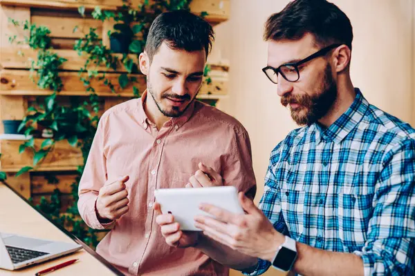 Genç hipster izlemenizi dijital tablet teknolojisiyle, işbirliği ve office coworking konuşurken touchpad hakkında bilgi proje için tarama erkekler birlikte sınavlarına hazırlık eğitimi