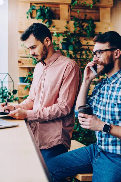 Genç gülümseyen hippi, iş arkadaşı bilgisayar ağlarından bilgi ararken erkek öğrenciler kahve molasında gerçek iletişimi görmezden geliyor.