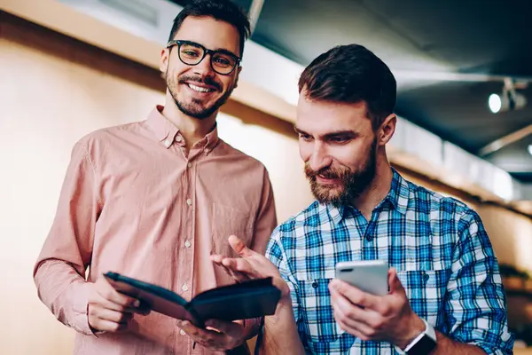 Neşeli yakışıklı erkek iş, ortak proje üzerinde birlikte samimi bir atmosferde işbirliği meslektaşım notlar üzerinde işaret hipster adam için planlama ile not defteri tutan kamera görüntülemenin portre