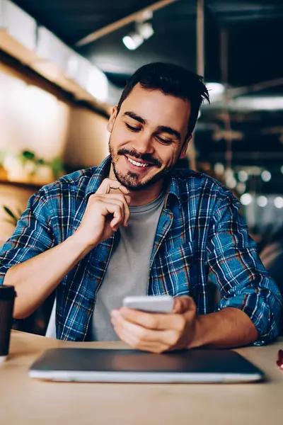 Sosyal ağlarda yeni mesajlar okuyan gülümseyen yenilikçi adam akıllı telefondan yeni bir arkadaşı doğruladı, cep telefonu bakiyesindeki bankacılık uygulamasından memnun olan genç adam öğrenirken cep telefonu bakiyesini kontrol ediyor.