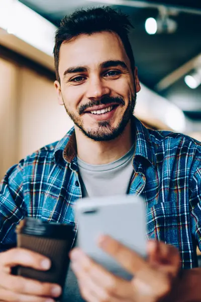 Takipçilerle sohbet etmek için telefonu kullanan ve sosyal medyadan zevk alan yeni arkadaşları onaylayan neşeli erkek blog yazarının portresi kahve molasında kameraya bakıp gülümseyen öğrenci