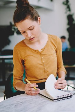 Üniversite kampüsünde oturmuş, ders kitaplarında bilgi arayan düşünceli bir kız öğrenci. Dağınık çörekleri olan dalgın, ciddi bir hippi kız masada oturuyor ve kafeteryada okuyor.