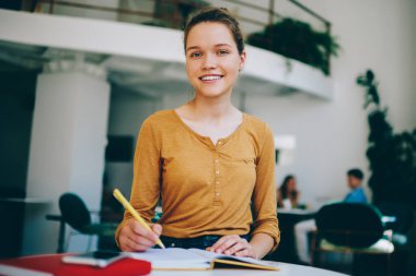 Kafeteryada boş vakit geçiren neşeli bayan gazeteci ve iş arasında kameraya bakan başarılı mutlu hippi kız üniversite kampüsünde ders çalışıyor ve sınava hazırlanıyor.