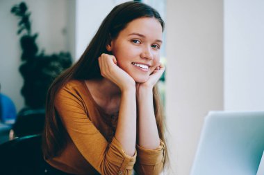 Üniversite kafeteryasında bilgisayar başında çalışırken yüzünde sevimli bir gülümsemeyle kameraya bakan başarılı kadın serbest yazar portresi. Kapalı alanda teknoloji kullanarak okuyan mutlu hippi kız.