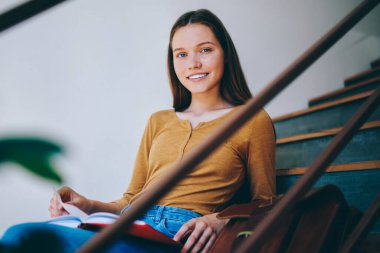 Mutlu başarılı öğrenci portresi, günlük kıyafetleriyle yağmurluklar ve boş zamanların tadını çıkaran üniversite kampüsünde kameraya bakan şık sırt çantalı bir kadın.