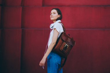 Çekici hippi kız duvarın yanında dikilirken düşünceli bakışlar atıyor. Sırt çantalı ve kulaklıklı 20 'li yaşlarda, duvar tanıtım alanının yanında dinleniyor.