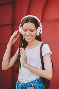 Yeni kulaklıkla müzik dinlemekten hoşlanan genç bir kız öğrenci ses kalitesinden tatmin olmuş gözlerini kapatıyor, kaygısız bir kadın dışarıda, duvarın yanında arkadaşını beklerken ses kitabı dinliyor.