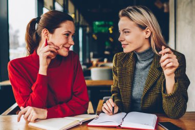 İki yaratıcı öğrenci işbirliği ile bloknot alan coworking içinde vasıl okul sırası oturan üretken strateji tartışıyor. Casual kıyafet birlikte ortak proje üzerinde çalışan kadın tasarımcılar gülümseyen