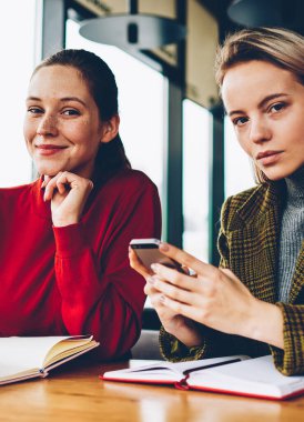 Yarım uzunluk portre iki başarılı tasarımcıların fikirler Smartphone cep telefonu ile arama ve kroki teamworking coworking içinde çizim yaparken kameraya bakıyor. Mobil ve olumlu öğrenci ile sarışın öğretmen