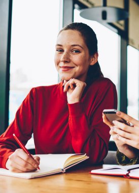 Yarım uzunluk portre iki başarılı tasarımcıların fikirler Smartphone cep telefonu ile arama ve kroki teamworking coworking içinde çizim yaparken kameraya bakıyor. Mobil ve olumlu öğrenci ile sarışın öğretmen