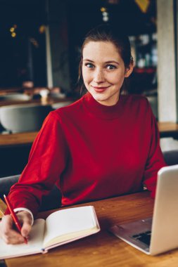 Kameraya gülümseyen ve modern dizüstü bilgisayar başında oturan Smartphone cep telefonu ile konuşurken arkadaş süre sınav hazırlama Not defterinizdeki notlar yapma sürpriz yetenekli öğrenci portresi için kablosuz 4 g bağlı