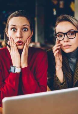 Yarım uzunluk portre merak iki yetenekli öğrencilerin üniversite web sitesinde indirilen sonuçları ile şok. Casual giyim kamera teamworking dizüstü bilgisayar, süre bakarak heyecanlı genç kadınlarda