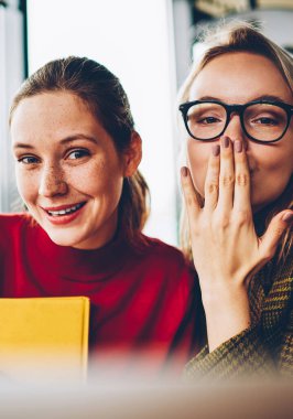 Sallanan el ile neşeli genç kadın ve Sarışın hipster öğrenci hava ile yarım uzunluk portre öpün kameraya gülümseyen. Mutlu güzel blogcular ile birlikte ücretsiz vakit duygusal ifadeler