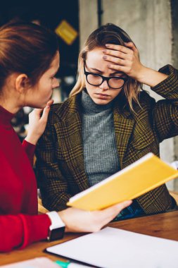 Nitelikli kadın öğretmen elinde yardımcı ders kitabı ile birlikte şık coworking alanda eğitim yaklaşan sınavlar için hazırlanması sırasında karışık eğitim malzeme anlamak için öğrenci depresif