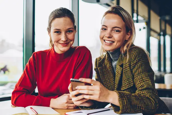 Kafede oturan smartphone yüklü yeni komik uygulama tartışırken kameraya gülümseyen iki mutlu blogcular portresi. Neşeli öğrenciler eğitim sırasında posta üstünde hareket eden telefon kontrol