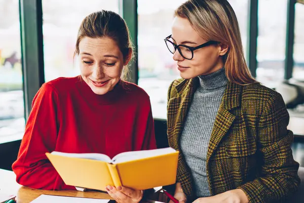 İki başarılı öğrencilere ders kitabı okuma ve birlikte coworking içinde oturan sınava hazırlık sırasında eğitim. Ciddi kadın öğretmen özel ders edebiyat ile iletken olumlu hipster kızla
