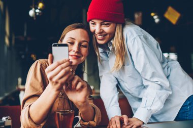 Neşeli iki hipsters smartphone aygıt komik video online izleme bağlı 4 g için Internet. Pozitif gençler sosyal ağlar üzerinde cep telefonu birlikte dinlenme kafe iç kontrol